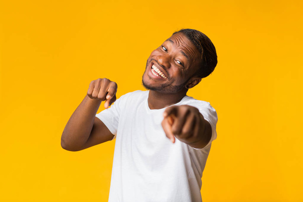 Χαμογελώντας μαύρος τύπος που δείχνει τα δάχτυλα στην κάμερα στέκεται, κίτρινο φόντο - Φωτογραφία, εικόνα