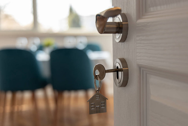 Yeni bir eve açılan kapı. Anahtarlı kapı kolu ve ev şeklindeki anahtarlık. İpotek, yatırım, gayrimenkul, mülk ve yeni konut kavramı - Fotoğraf, Görsel