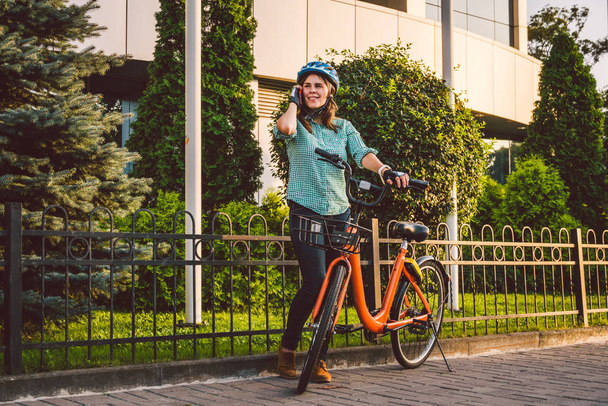 Porträt eines fröhlichen Mädchens, das sein Handy in der Hand hält. Glücklich lächelnder Student mit Fahrrad-Sharing-App auf dem Smartphone im Freien. Stilvolles Hipster-Mädchen mit Fahrrad per Smartphone-App auf der Straße - Foto, Bild