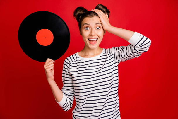 Retro discotheque concept. Amazed funny funky girl hold vinyl plate impressed scream wow omg wear striped white sweater isolated red color background - 写真・画像