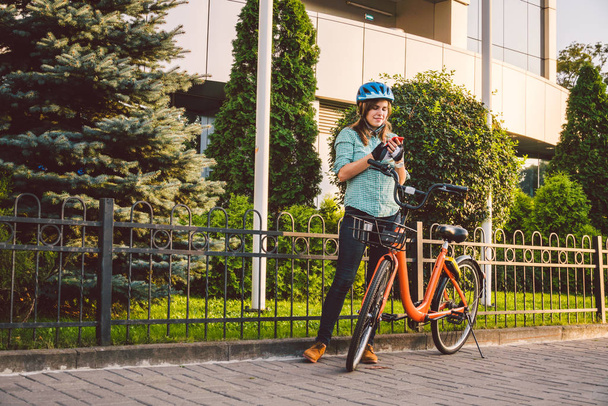 Портрет веселої дівчини, що тримає мобільний телефон. Щасливий усміхнений студент використовує додаток для обміну велосипедами на смартфоні на відкритому повітрі. Міський спосіб життя стильна дівчина-хіпстер з велосипедом, використовуючи додаток для смартфона на вулиці
 - Фото, зображення