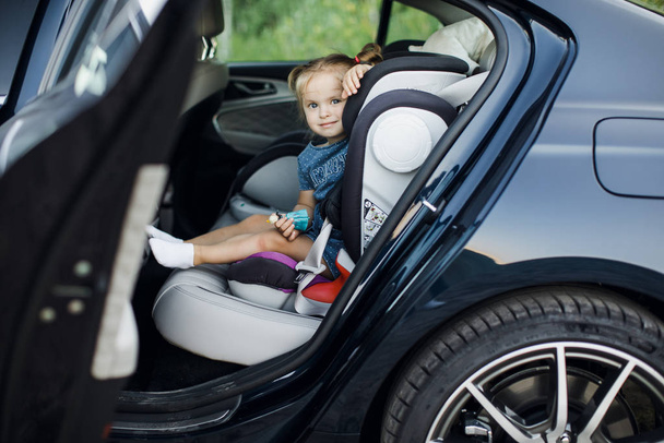 Το κοριτσάκι κοιτάει από το παράθυρο του αυτοκινήτου. μικρό κορίτσι κάθεται σε ένα παιδικό κάθισμα στο αυτοκίνητο - Φωτογραφία, εικόνα