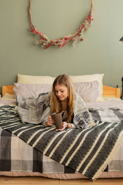Красива жінка на ліжку під плед п'є чай. Сучасний і стильний дизайн кімнати
. - Фото, зображення