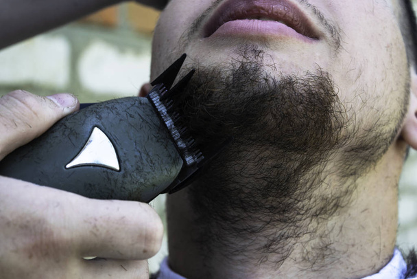 der Friseur schneidet einem Typen mit Schermaschine seinen Bart - Foto, Bild