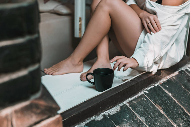Woman in white dress is sitting on the windowsill with big black tea cup. Morning concept. - Foto, immagini