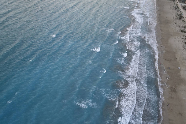 Fehér habos tengeri hullámok fröcskölnek a homokos strandra este. Esti szörfözés. Légi felvétel az Uav drónról - Fotó, kép