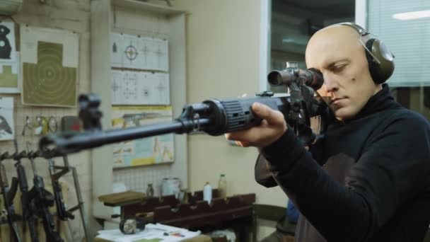 Um homem em fones de ouvido olha para a visão óptica de um rifle sniper
 - Filmagem, Vídeo