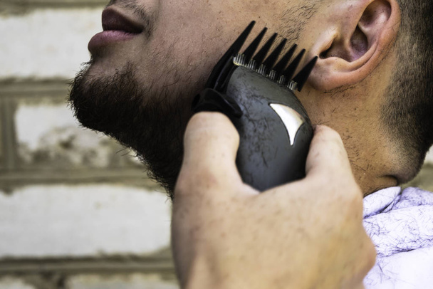 de kapper snijdt zijn baard aan een man met een schaarmachine - Foto, afbeelding