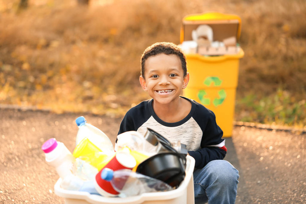 Little African-American boy collecting trash outdoors. Concept of recycling - Photo, image
