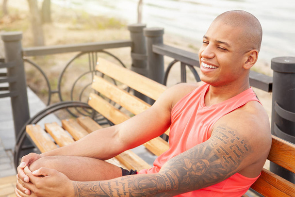 Handsome athletic African man laughing joyfully resting outdoors - Photo, Image