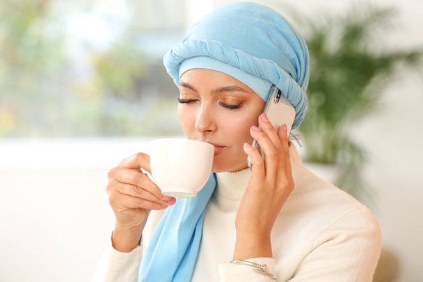 Portrait of beautiful Muslim woman talking by phone while drinking tea at home - Photo, Image