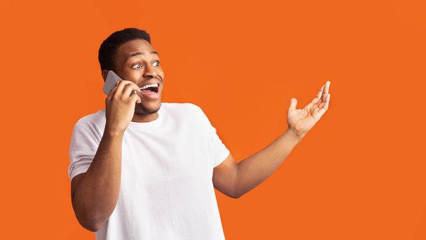 Zaskoczony czarny facet rozmawiający przez telefon i gestykulujący - Zdjęcie, obraz