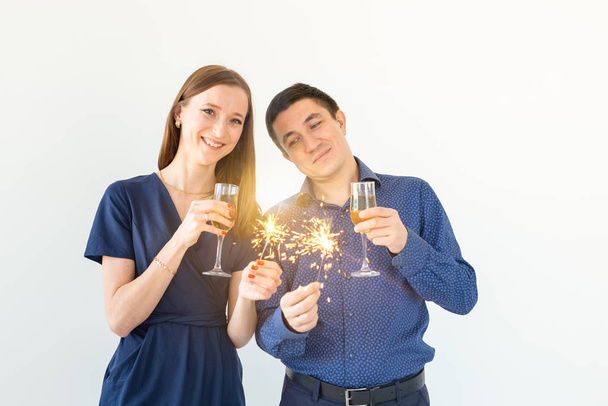 Άνδρας και γυναίκα γιορτάζουν τα Χριστούγεννα ή την παραμονή της Πρωτοχρονιάς κόμμα με φώτα της Βεγγάλης και ποτήρια σαμπάνιας σε λευκό φόντο. - Φωτογραφία, εικόνα
