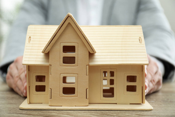 Real estate agent holding house model at wooden table, closeup - Foto, imagen