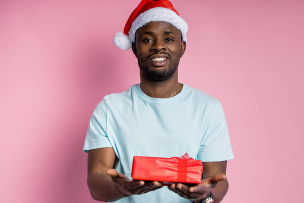 Young african american man wearing Santa hat holding gift - Photo, image