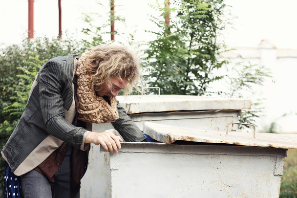 Poor homeless man looking for food in garbage toter outdoors - Foto, Bild