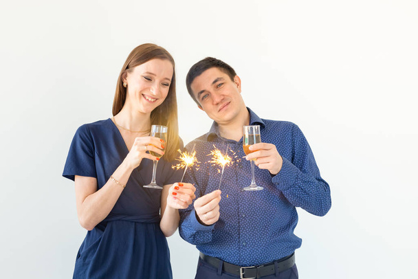 Man and woman celebrating Christmas or New Year eve party with Bengal lights and glasses of champagne on white background. - Fotó, kép