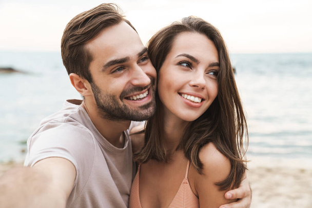 Photo of smiling young couple hugging and taking selfie photo - Fotó, kép