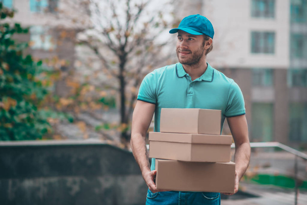 Handsome bearded delivery man wearing t-shirt holding boxes - Fotografie, Obrázek