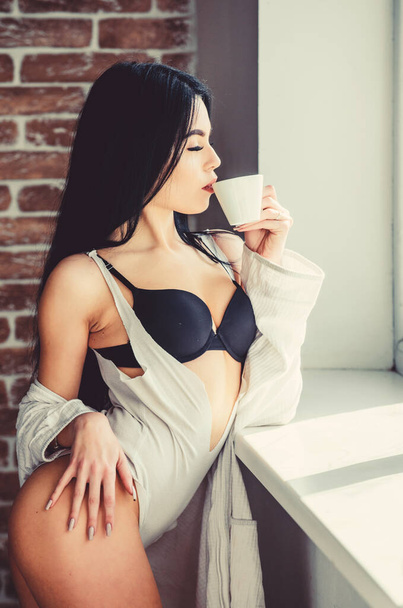 Coffee in the morning giving her the mood. Sensual girl enjoying her aromatic morning coffee. Sexy woman drinking healthy morning drink at window. Coffee wakes her up in the morning - Foto, Imagem