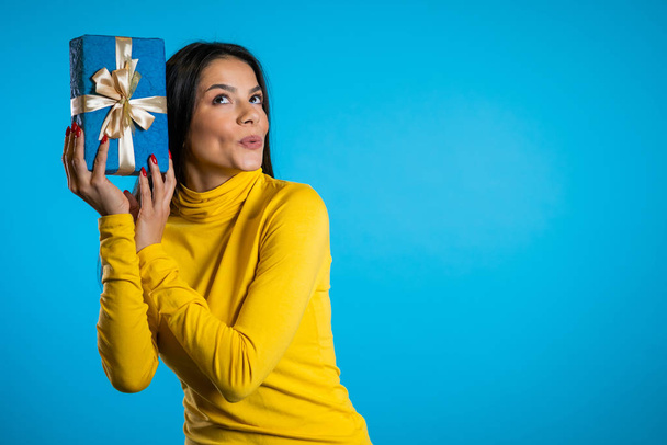 Pretty woman received gift box and interested in whats inside. She is happy and flattered by attention. Girl on blue background. - Valokuva, kuva