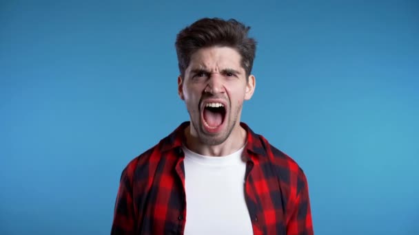 Jong europees gestrest man in rood shirt schreeuwen geïsoleerd over blauwe achtergrond - Video