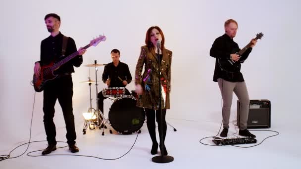 Een muzikale band van vier mensen in zwarte kleren die een lied spelen in de heldere studio - een vrouw die een gouden jurk draagt - Video
