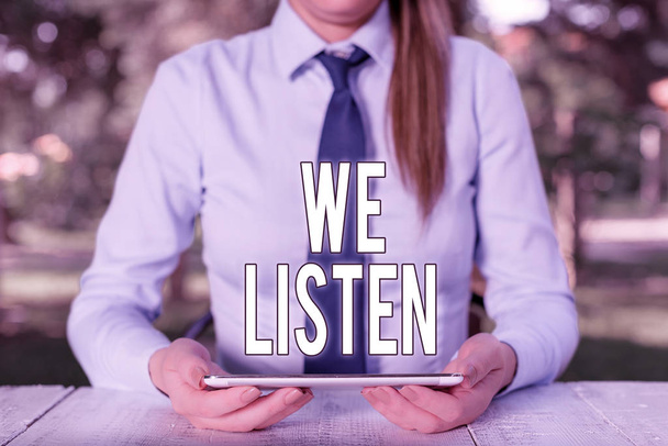 Writing note showing We Listen. Business photo showcasing Group of showing that is willing to hear anything you want to say Female business person sitting by table and holding mobile phone. - Photo, Image