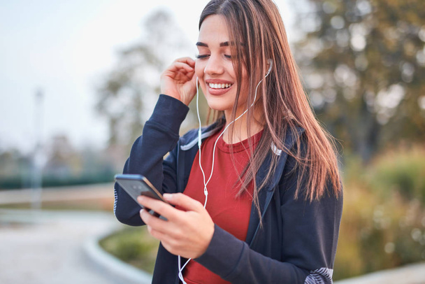 Mujer joven moderna con teléfono celular haciendo una pausa durante el jogging /
  - Foto, Imagen