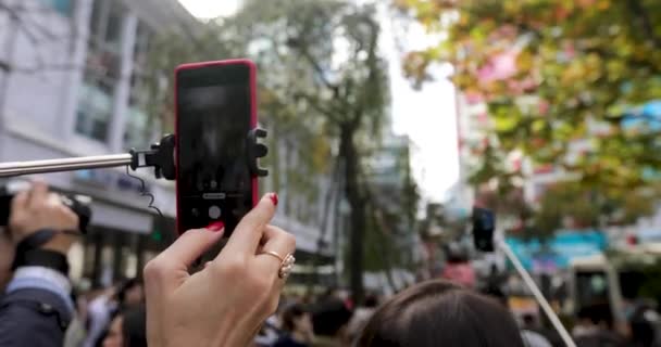 Osoba fotografowania na smartfonie na selfie kij na ulicy - Materiał filmowy, wideo