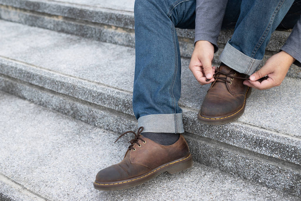 gens homme en jeans attacher lacet sur le port de chaussures en cuir marron assis escalier fond. Style de vie des hommes. Laisser de la place pour l'écriture de texte descriptif
. - Photo, image