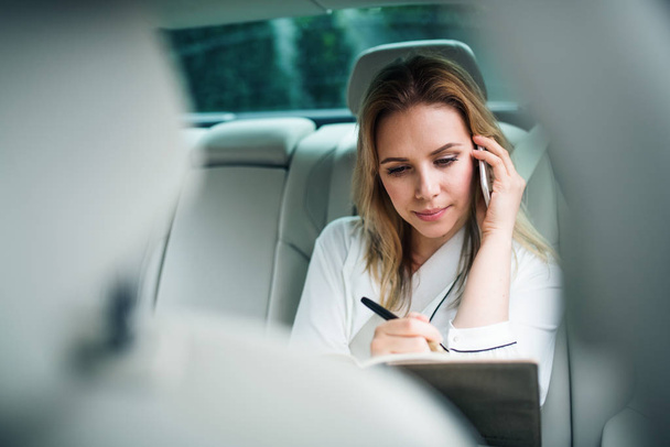 Geschäftsfrau mit Smartphone sitzt im Taxi auf Rücksitzen. - Foto, Bild