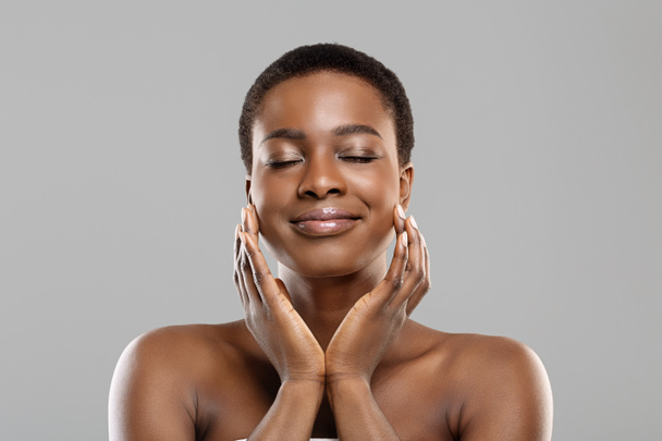 Портрет красивой афро-девушки, касающейся своей идеальной кожи на лице
 - Фото, изображение