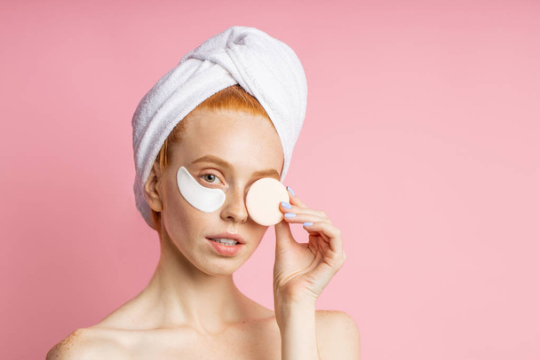 Shot of young woman applies eye patches and holding cosmetic sponge - 写真・画像
