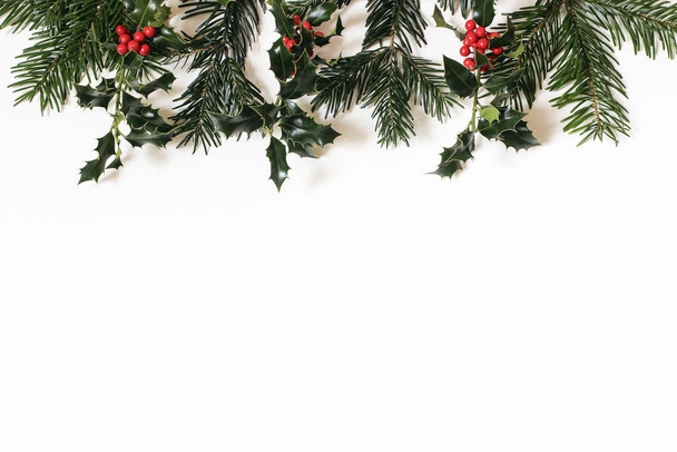 Cornice floreale natalizia, banner web. Confine di bacche di agrifoglio rosso e rami di abete verde isolati su sfondo bianco tavolo. Decorazione naturale invernale, ghirlanda. Botanico festivo piatto lay, vista dall'alto
 - Foto, immagini