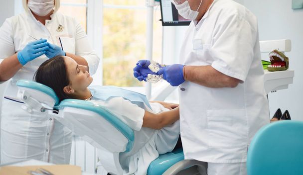 Lekarz dentysta leczy zęby pięknej młodej dziewczyny pacjenta. - Zdjęcie, obraz