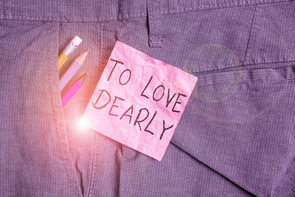 Text sign showing To Love Dearly. Conceptual photo Love someone very much in the more humble way and aimlessly Writing equipment and pink note paper inside pocket of man work trousers. - 写真・画像
