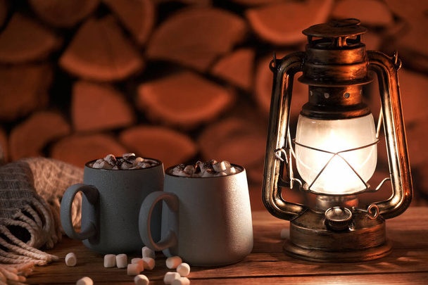 The antique oil lamp and mugs with hot cocoa on the firewood background. - Photo, Image