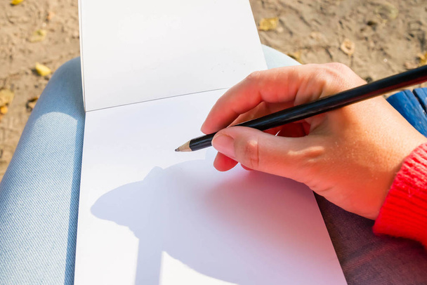Un bloc de notas en blanco para la planificación, resumiendo. La mano sostiene el lápiz. Ella dibujará o guardará un bloc de notas
. - Foto, Imagen