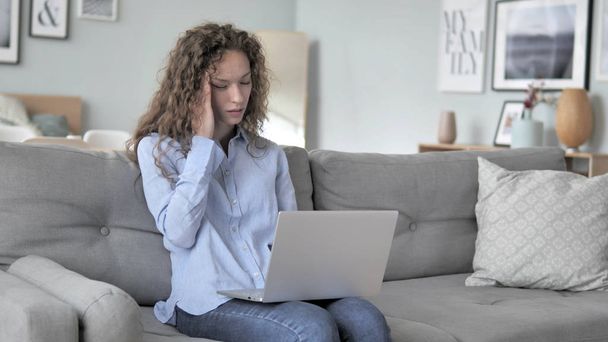 Curly Hair Woman com dor de cabeça trabalhando no laptop enquanto sentado no sofá
 - Foto, Imagem
