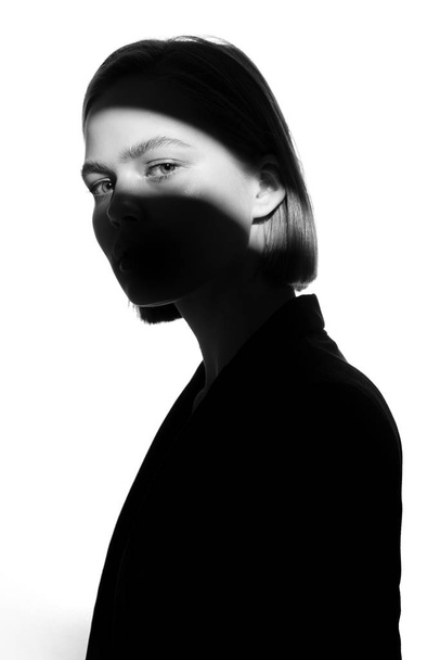Fashionable beauty portrait. Black silhouette on white background. Girl with a spot of light on her face.  - Zdjęcie, obraz