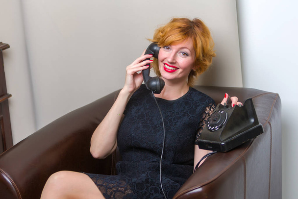 Portrait of young woman talking using a vintage telephone agains - Photo, image