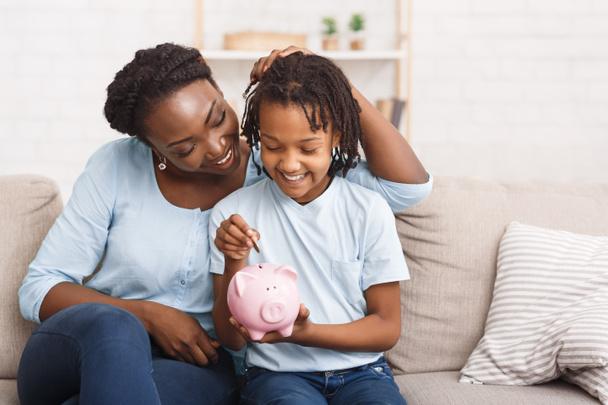 Pieni musta tyttö laittaa rahaa säästöpossu
 - Valokuva, kuva