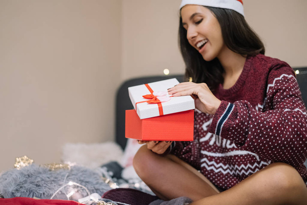 Woman wearing Santa hat opening gift in bed - Foto, imagen