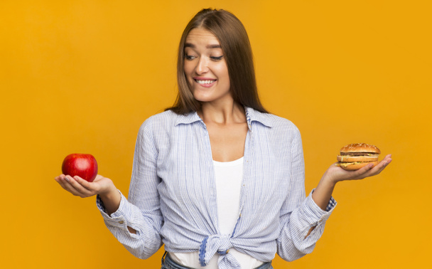 Hladová žena výběr mezi jablkem a hamburger stojící ve studiu - Fotografie, Obrázek