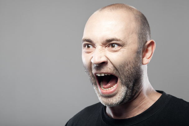 Dühös ember sreaming szürke háttérrel, elszigetelt portréja - Fotó, kép