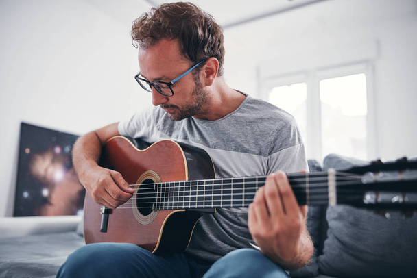 Человек, играющий на акустической гитаре в гостиной
. - Фото, изображение