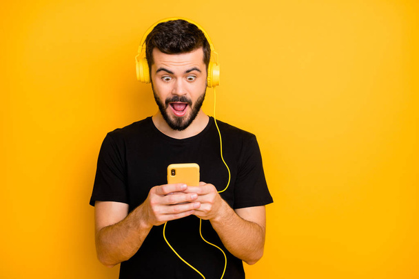 Omg super hit. Amazed surprised guy listen music use headset search sound track on his smartphone find unbelievable song scream wear good looking outfit isolated over yellow background - Fotoğraf, Görsel