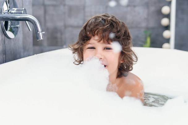 Funny little boy plays with foam in a bath. - Foto, Imagen