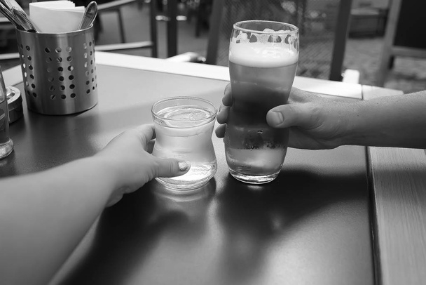 a glass of water and beer in the hands of a couple at a table - 写真・画像